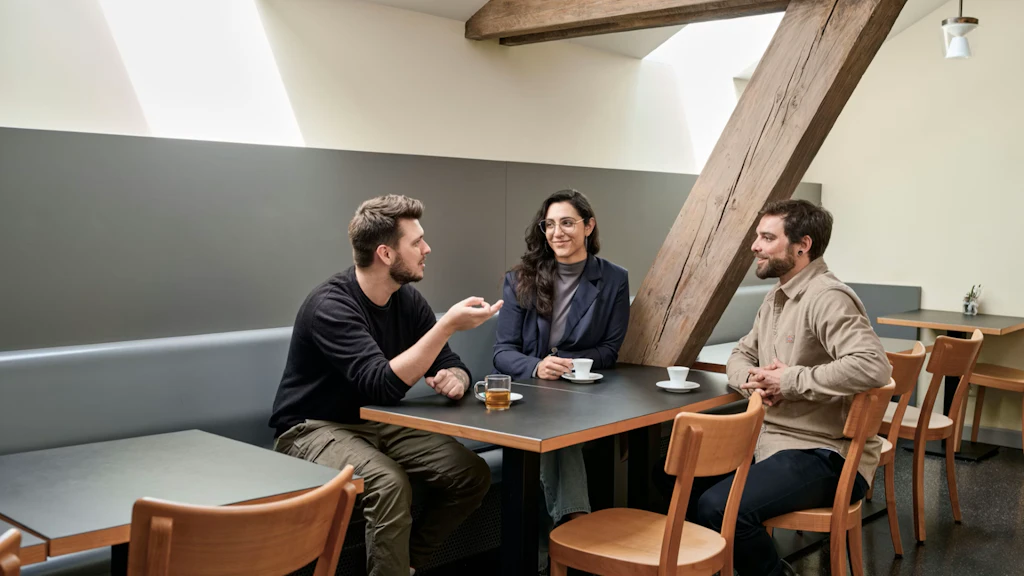 Zwei Männer und eine Frau hocken an einem Tisch und trinken Kaffee.